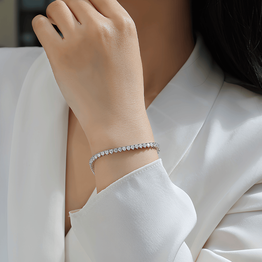 A close-up of a person wearing a delicate silver tennis bracelet with clear stones, styled with a white satin blouse.
