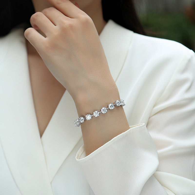 A close-up of a woman wearing a silver-toned tennis bracelet with clear round-cut stones, styled with a white blazer.