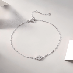A delicate silver chain bracelet with a small pavé-set eye charm, displayed on a light gray textured surface.