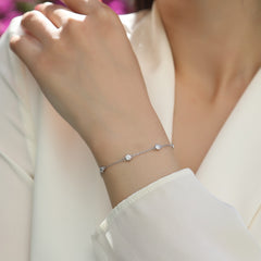 A delicate silver chain bracelet with three small clear gemstones worn on a woman's wrist, shown against a soft cream-colored blouse.