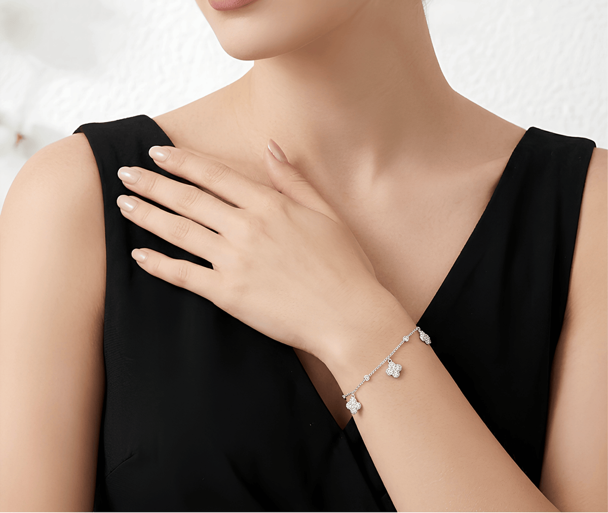 A close-up of a woman wearing a delicate silver bracelet with small floral charms, styled with a black sleeveless top.