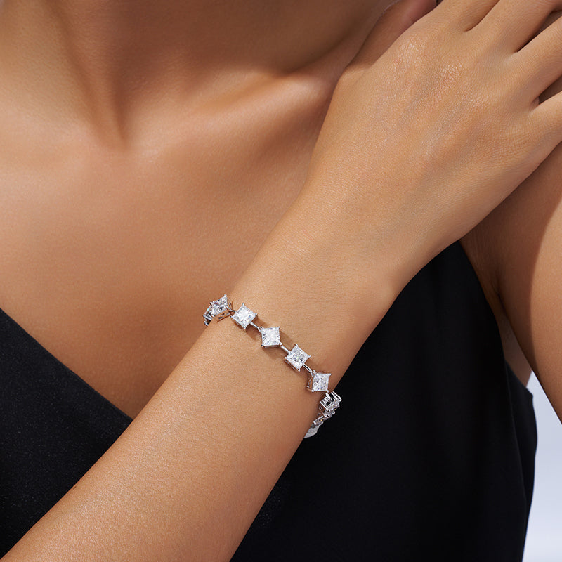 A silver tennis bracelet featuring clear, bezel-set princess-cut crystals arranged in a repeating pattern, shown against a plain white background.
