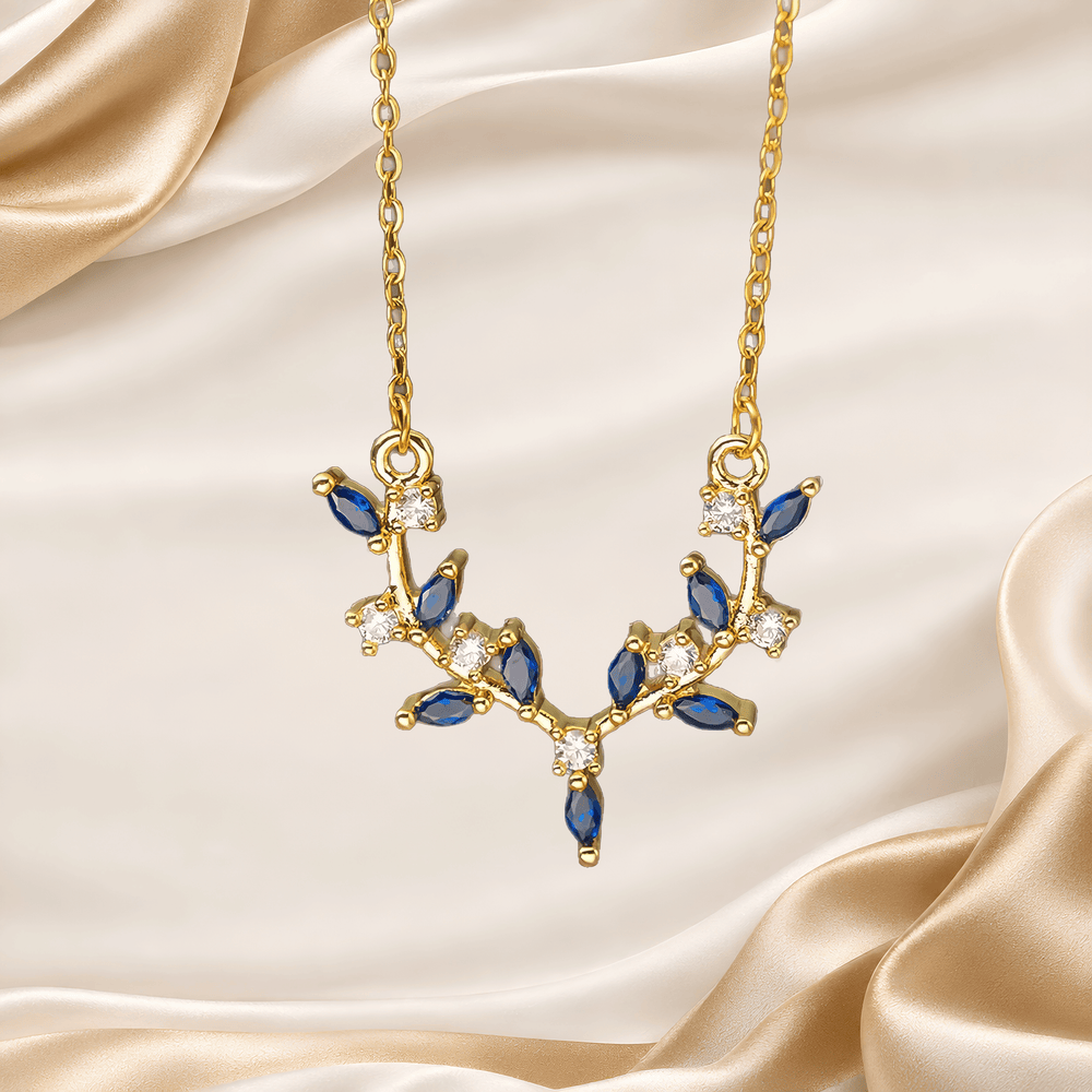 Gold branch-shaped necklace with blue marquise-cut stones and clear round stones, displayed on draped champagne satin fabric.