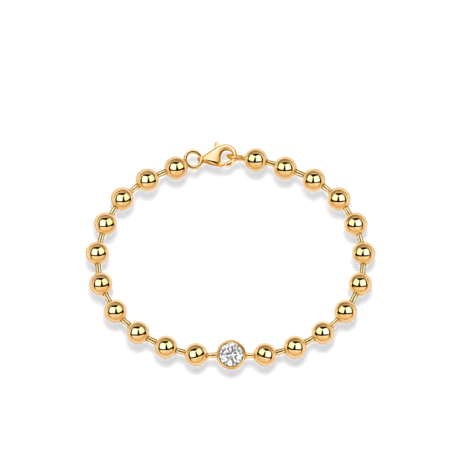 A gold beaded bracelet with a single round clear gemstone accent, displayed on a clean white background.