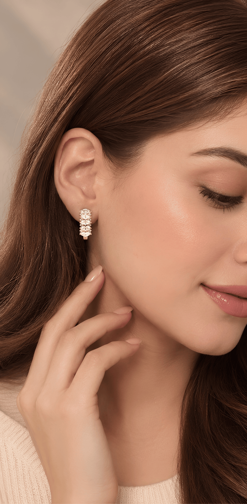 A close-up of a woman wearing a delicate gold hoop earring adorned with small clear stones, shown against her ear and hair.