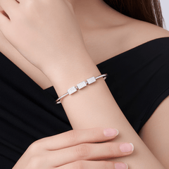 A close-up of a woman's wrist wearing a slim silver cuff bracelet with three rectangular clear stone clusters, against a black top background.