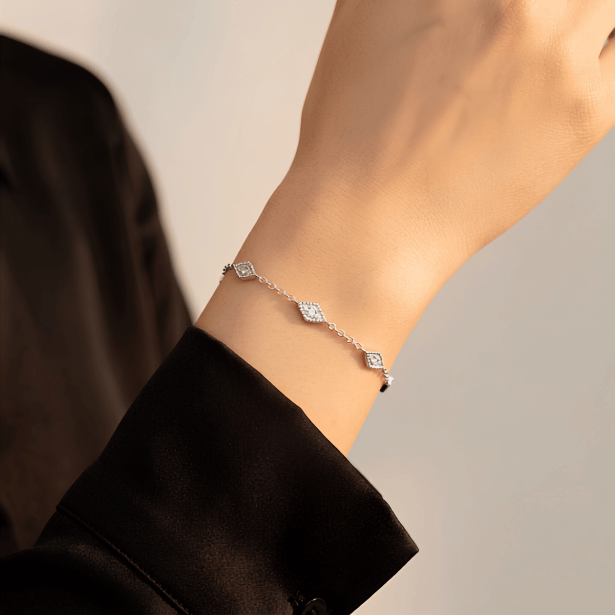 A delicate silver chain bracelet with three small diamond-shaped clear stone charms, shown worn on a person's wrist against a soft light gray background.