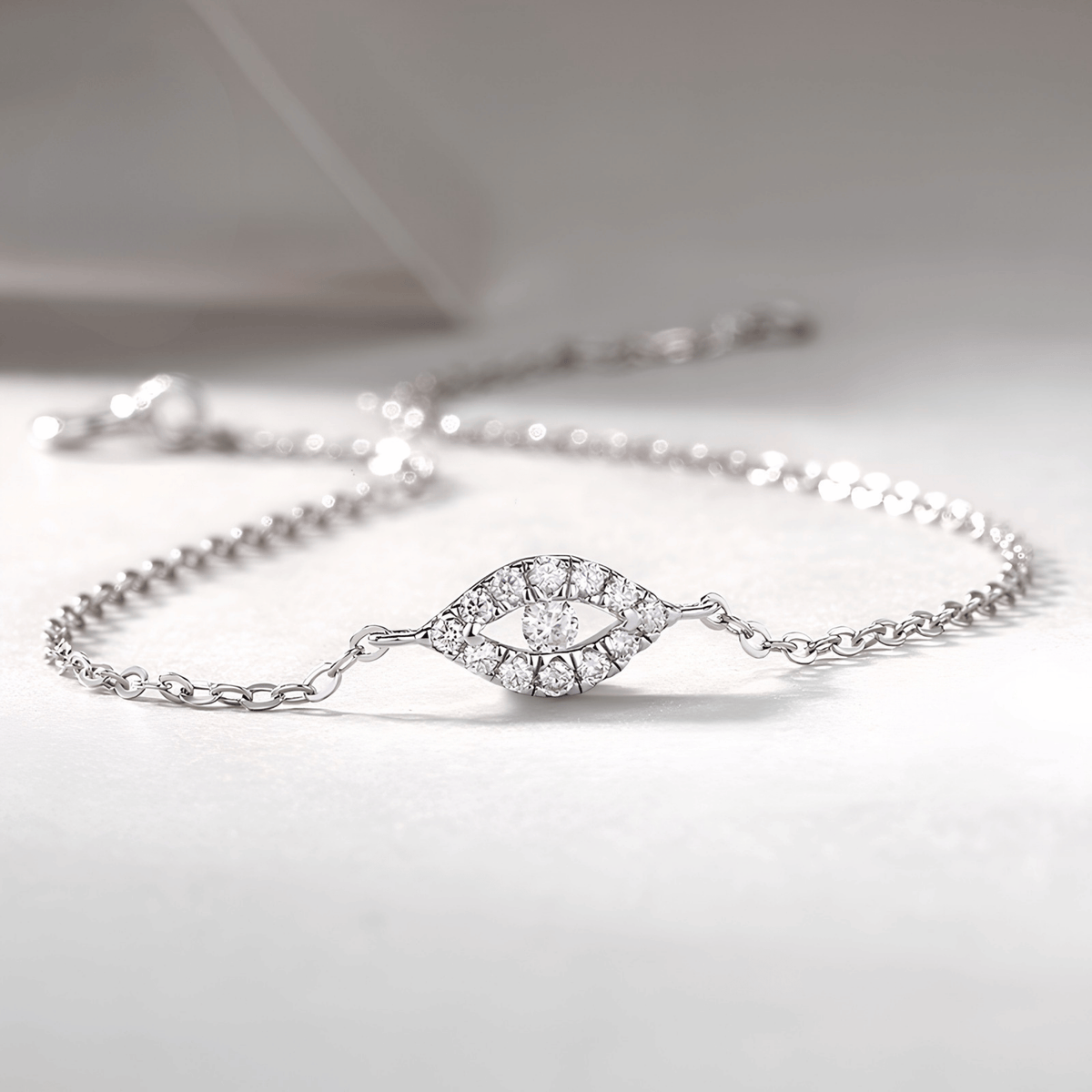 A delicate silver chain bracelet featuring an eye-shaped centerpiece paved with small clear stones, displayed on a soft light gray surface.