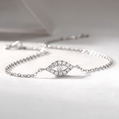 A delicate silver chain bracelet featuring an eye-shaped centerpiece paved with small clear stones, displayed on a soft light gray surface.