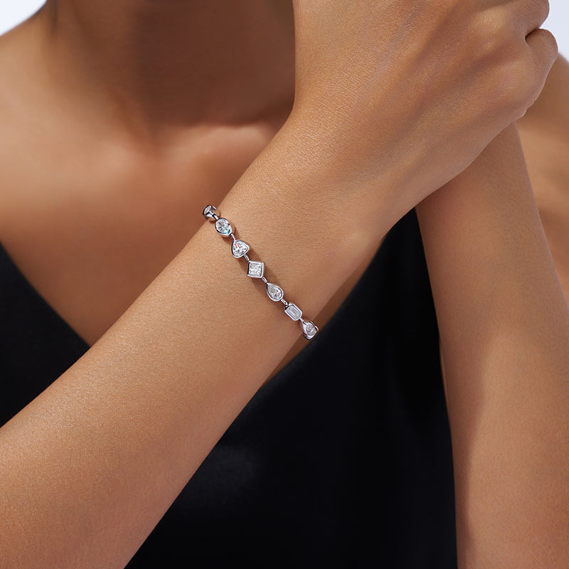 A close-up of a delicate silver bracelet with clear faceted gemstones worn on a woman's wrist. The bracelet features a repeating pattern of geometric and heart-shaped clear stones set in silver.