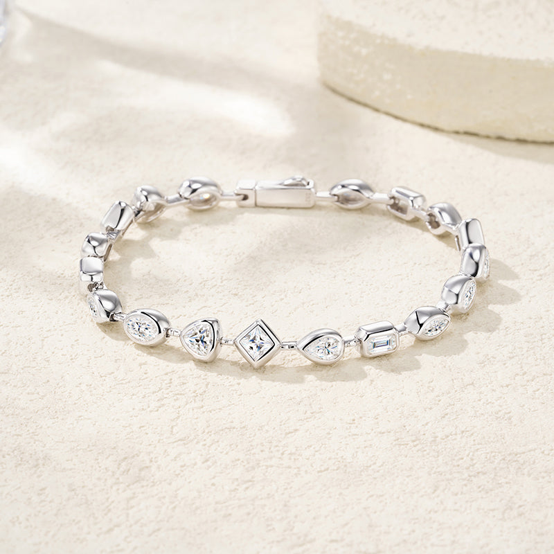 A silver link bracelet with heart and diamond-shaped links, some set with clear stones, displayed on a textured beige surface.