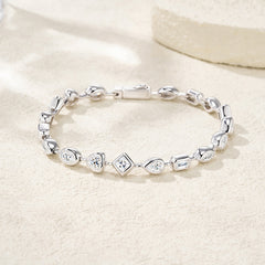 A silver link bracelet with heart and diamond-shaped links, some set with clear stones, displayed on a textured beige surface.