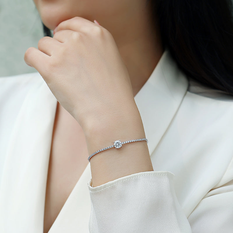 A close-up of a woman wearing a delicate silver-toned bracelet with a single round clear gemstone on her wrist, paired with a white blazer.