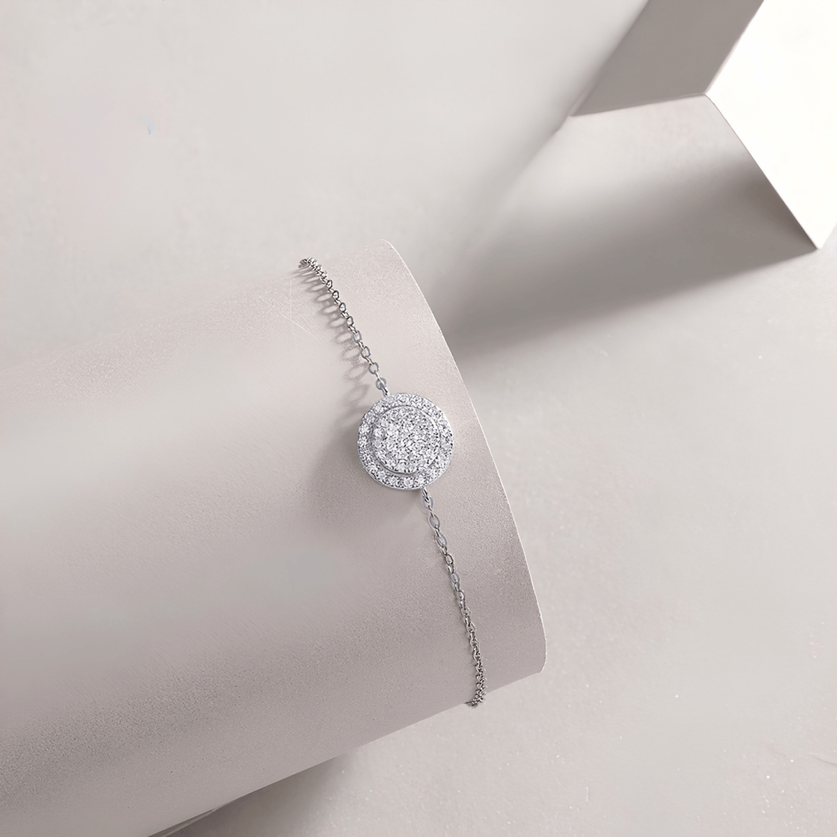 A delicate silver bracelet with a round pavé moissanite bracelet, displayed on a light gray jewelry stand.