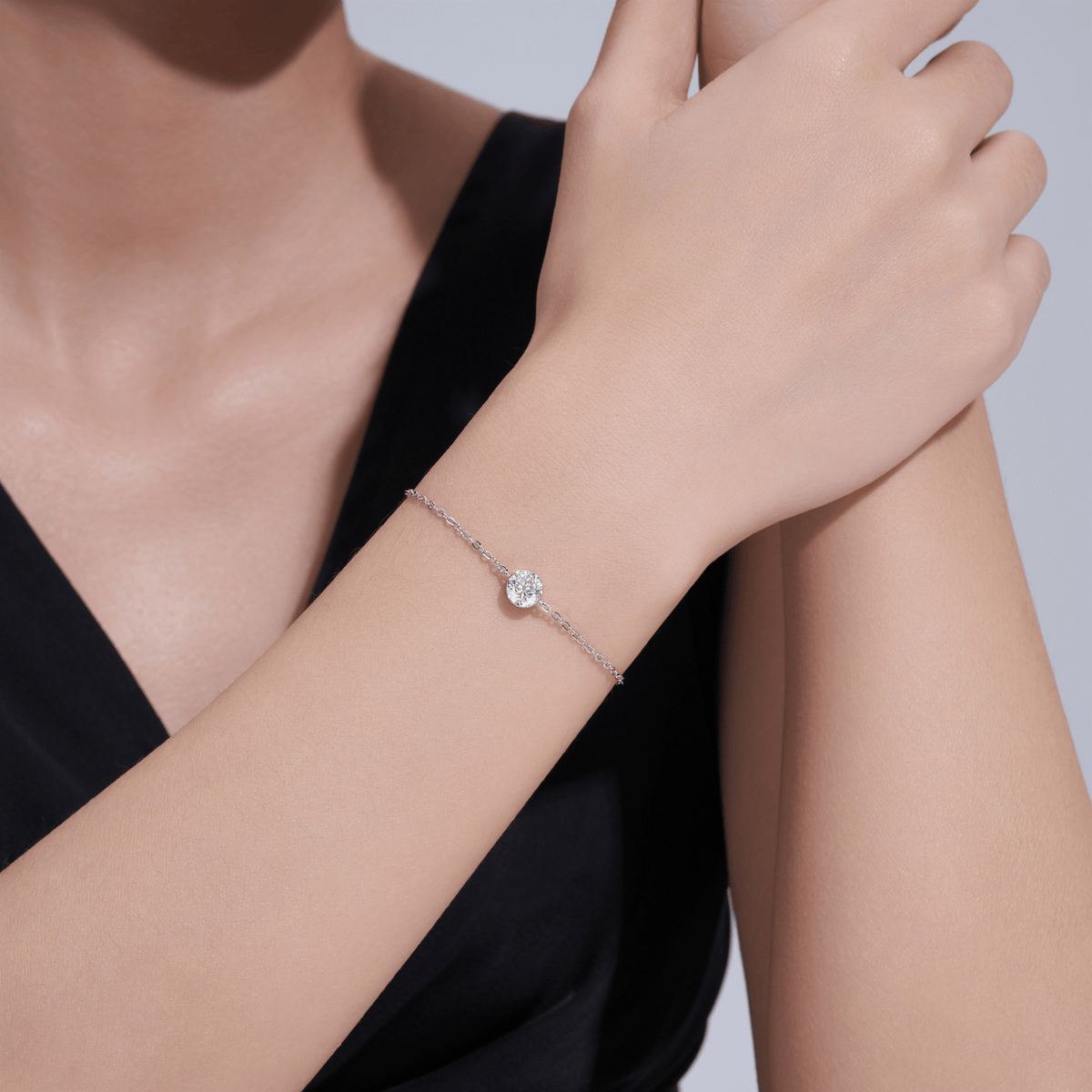 A delicate silver chain bracelet with a single round clear gemstone, shown worn on a woman's wrist. The model is wearing a black top against a light gray background.