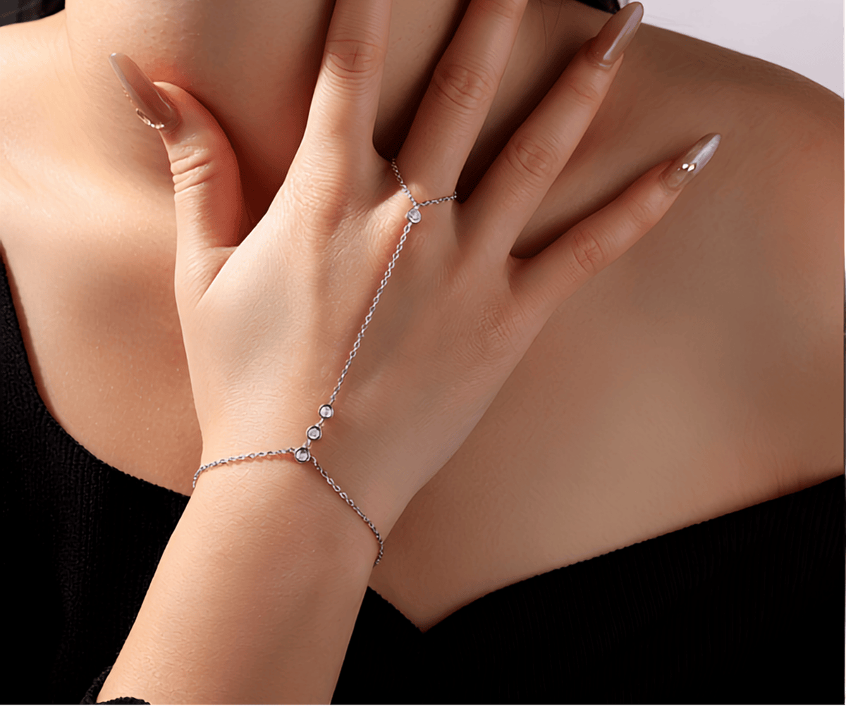 A delicate silver chain hand bracelet with a matching ring, worn on a model's hand and wrist. The jewelry features small clear rhinestones and is shown against the model's shoulder and neck.