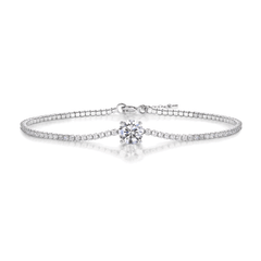 A silver-toned tennis bracelet featuring a central round-cut clear gemstone and a row of small pavé-set stones along the band, shown on a clean white background with a soft reflection.