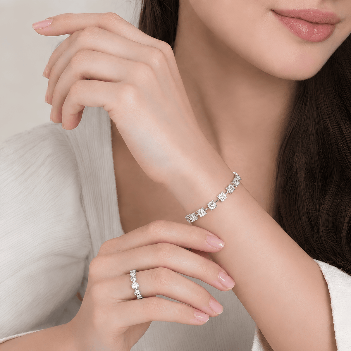 A close-up lifestyle shot of a woman wearing a delicate silver tennis bracelet on her wrist and a matching silver ring on her finger. The jewelry features small, sparkling round-cut stones set in a polished silver-toned metal.