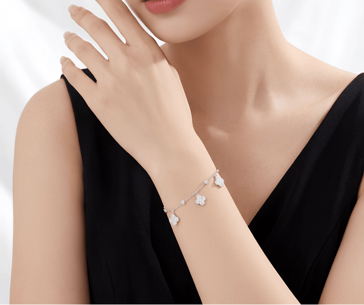A close-up of a model wearing a delicate silver chain bracelet adorned with small white flower charms, paired with a black sleeveless top.
