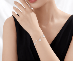 A close-up of a model wearing a delicate silver chain bracelet adorned with small white flower charms, paired with a black sleeveless top.
